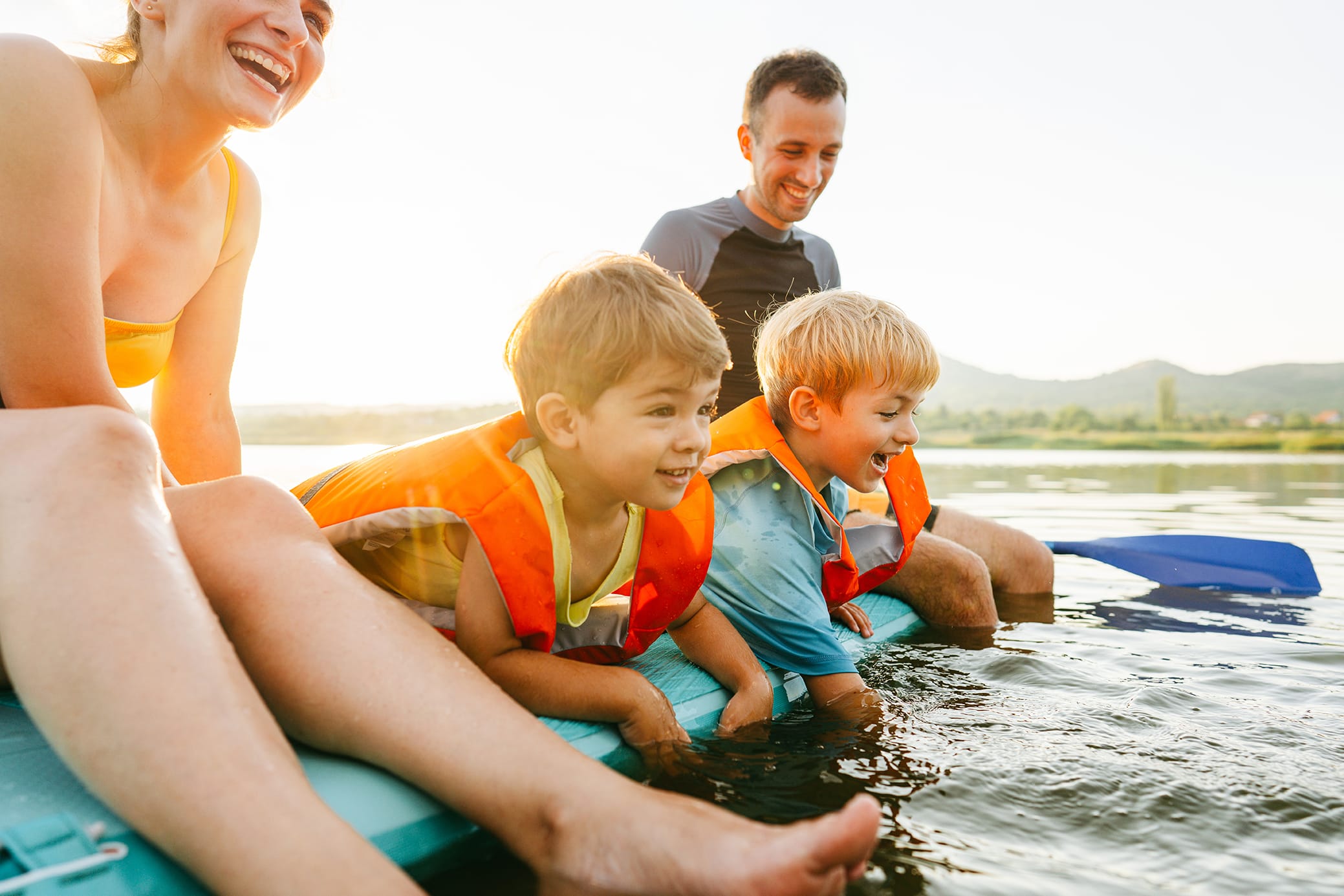 Albright Land & Development at Cedar Creek Lake | Mother and father sit on a paddleboard in the lake with their two young boys in lifejackets. The boys are laughing and splashing in the lake water.